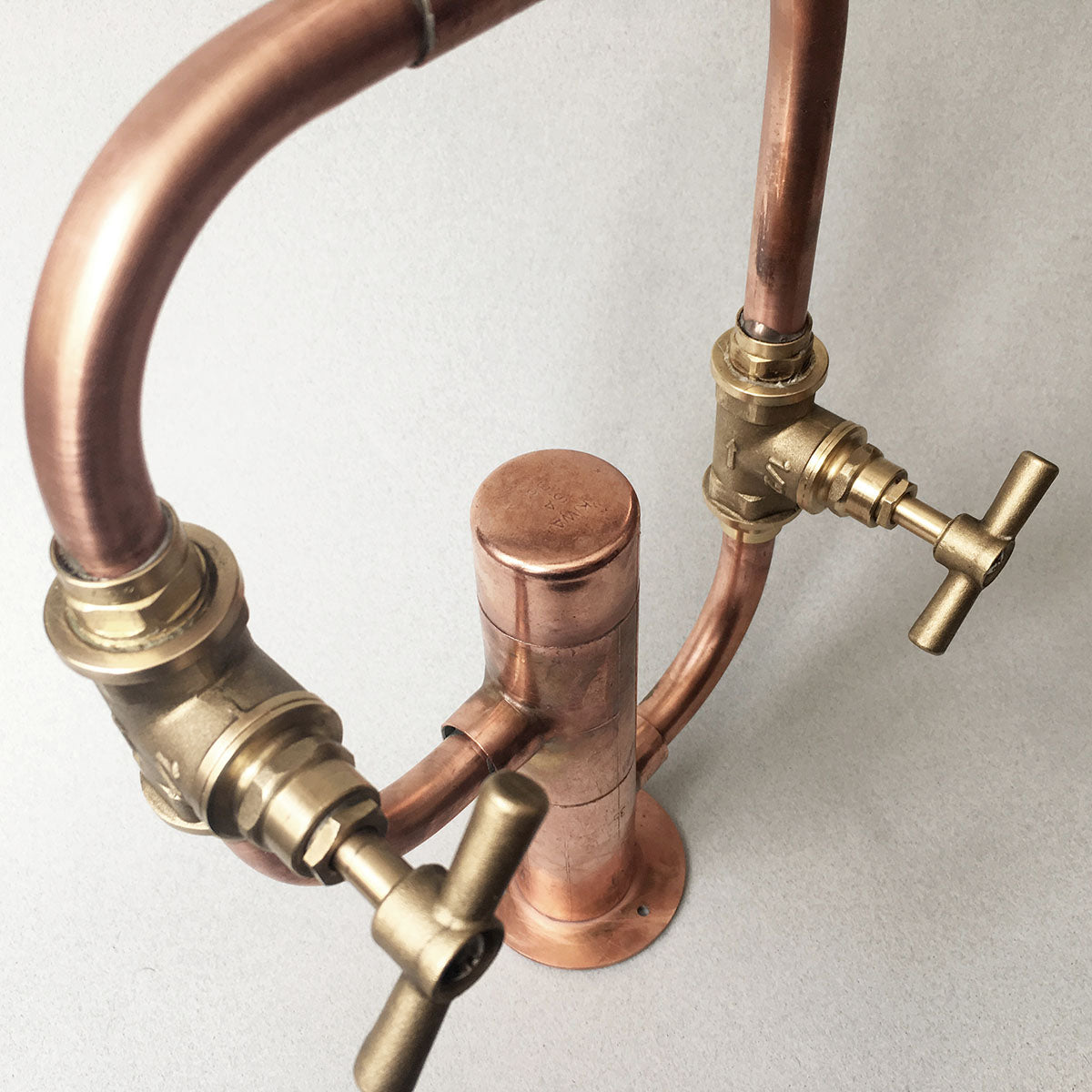 Pedestal Diagonal is a copper and brass deck-mounted sink faucet by Switchrange, featuring exposed piping and a striking brutalist design for indoor or outdoor settings.