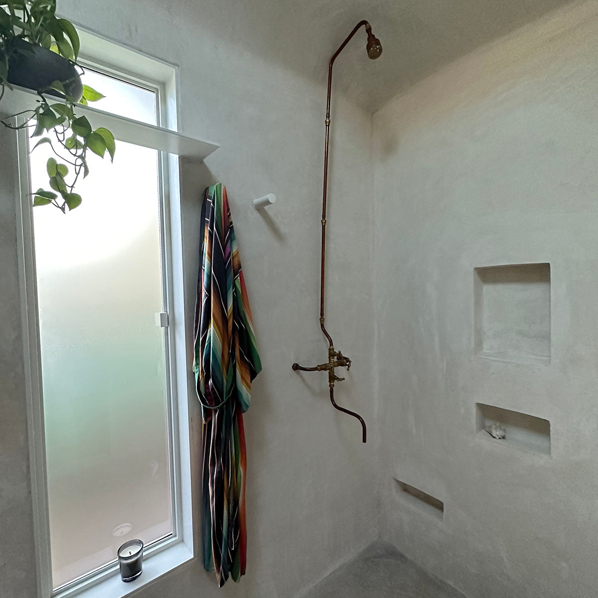 Copper shower with foot wash in brutalist style bathroom by Switchrange